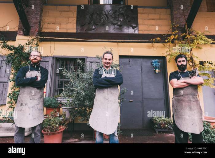 Portrait of three male metalworkers with arms folded outside forge ...
